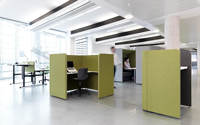 A green and white office with office work booths, desks and chairs.