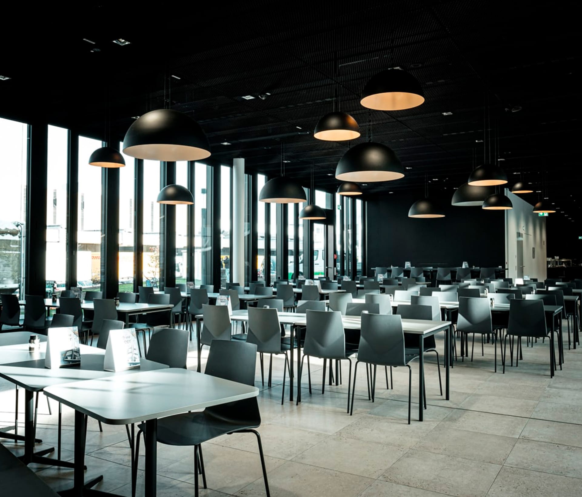 A large canteen full of canteen furniture such as black tables and chairs.