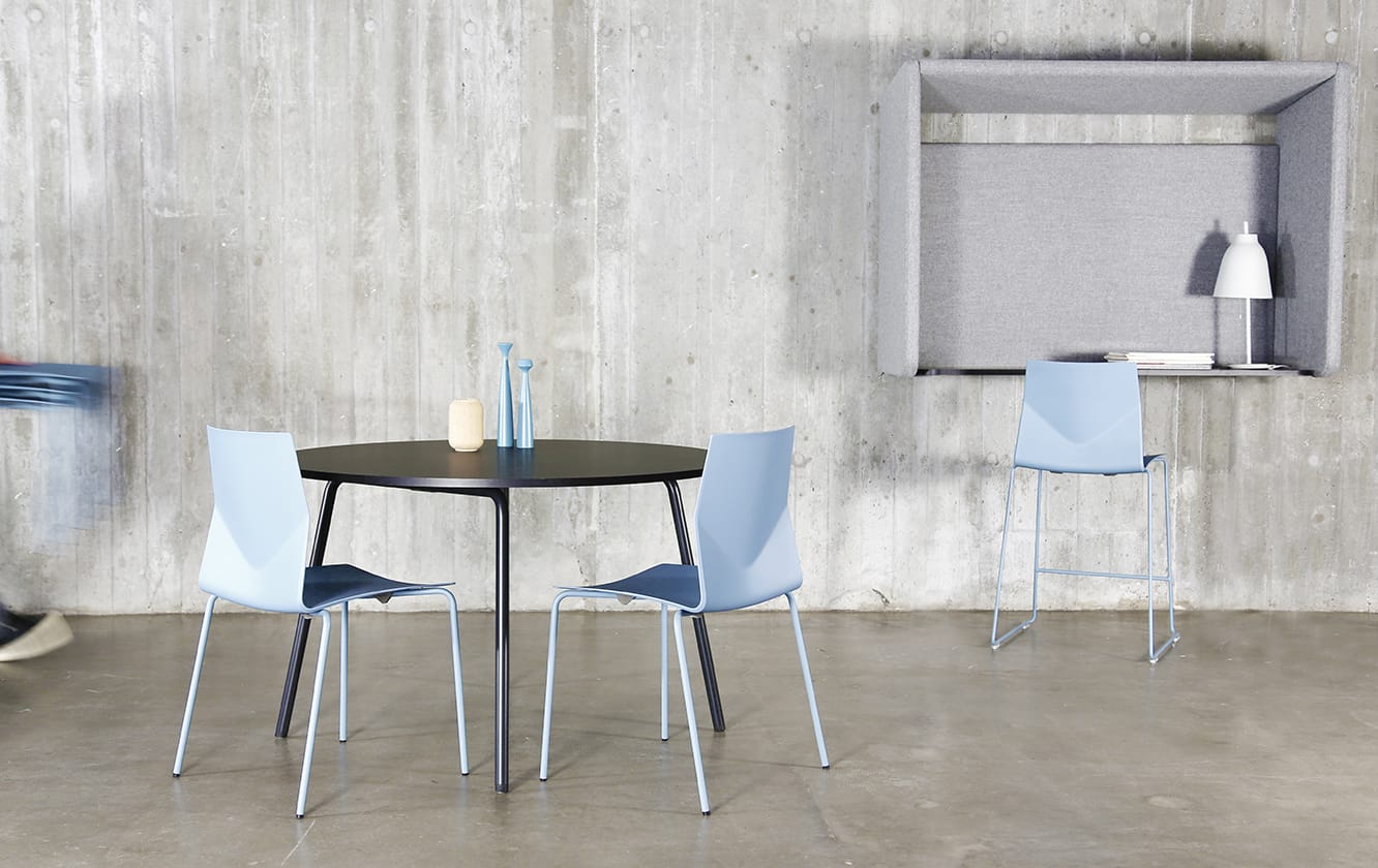 A table and chairs in a room with a concrete wall with a wall mounted desk workstation on the wall.