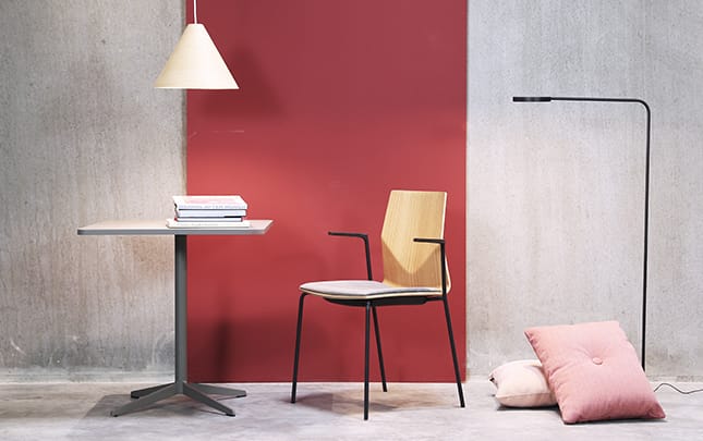 A table, chair and lamp in a room with a red wall.