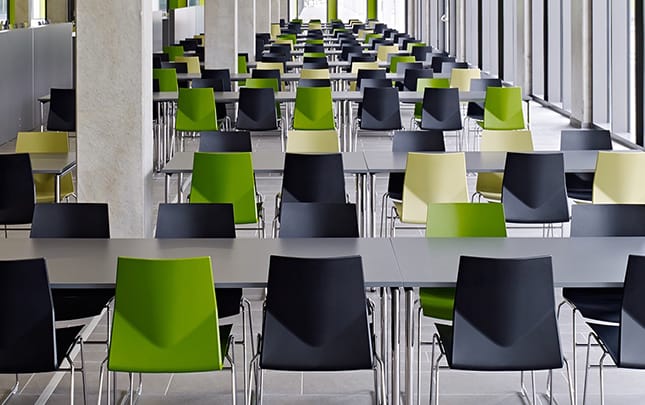 A long line of black and green chairs in a large room with office tables.