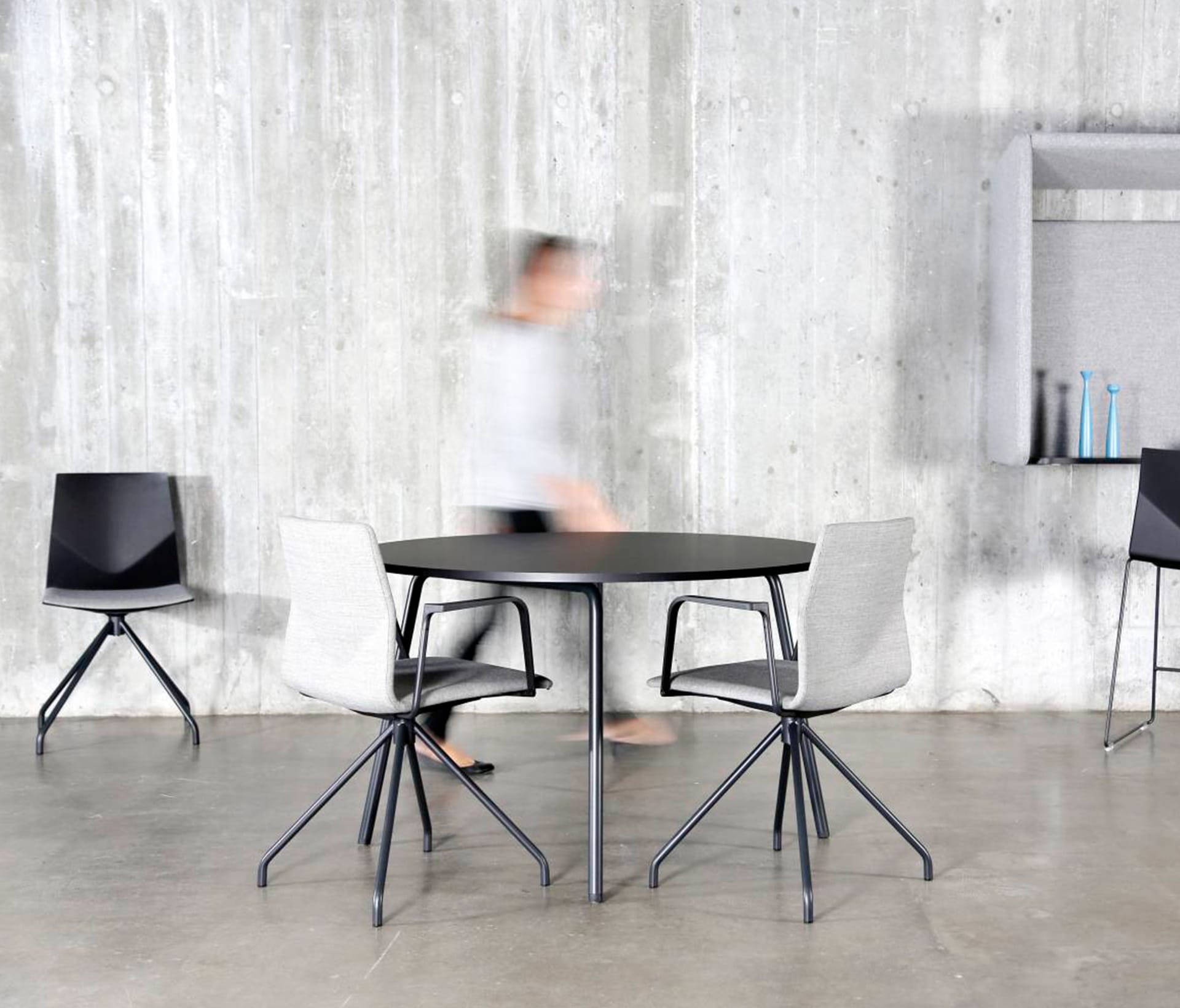 A person walks past a table and chairs in a concrete room.