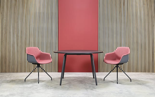 Two pink chairs and a table in front of a red wall.