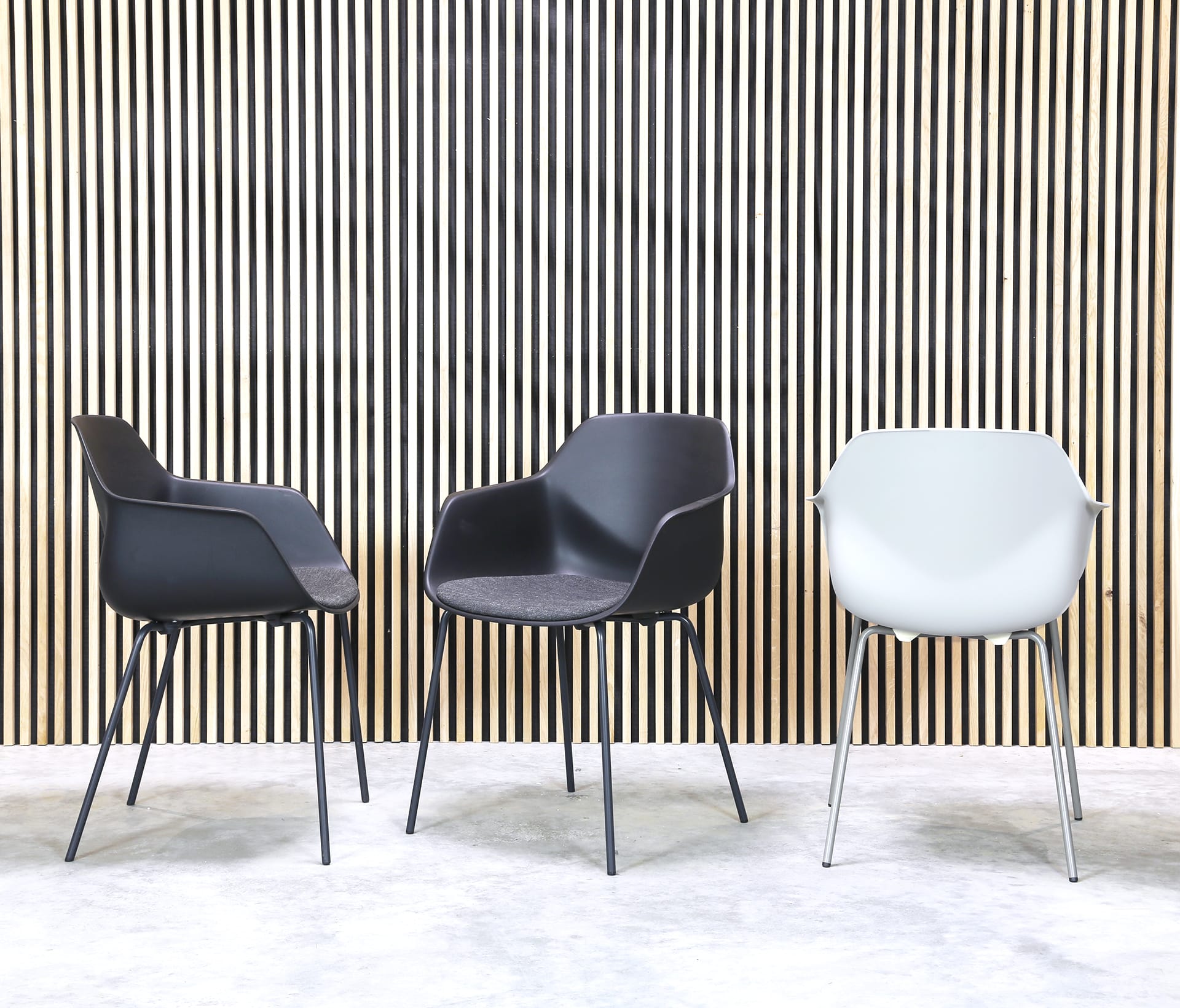 Three black and white chairs in front of a wooden wall.