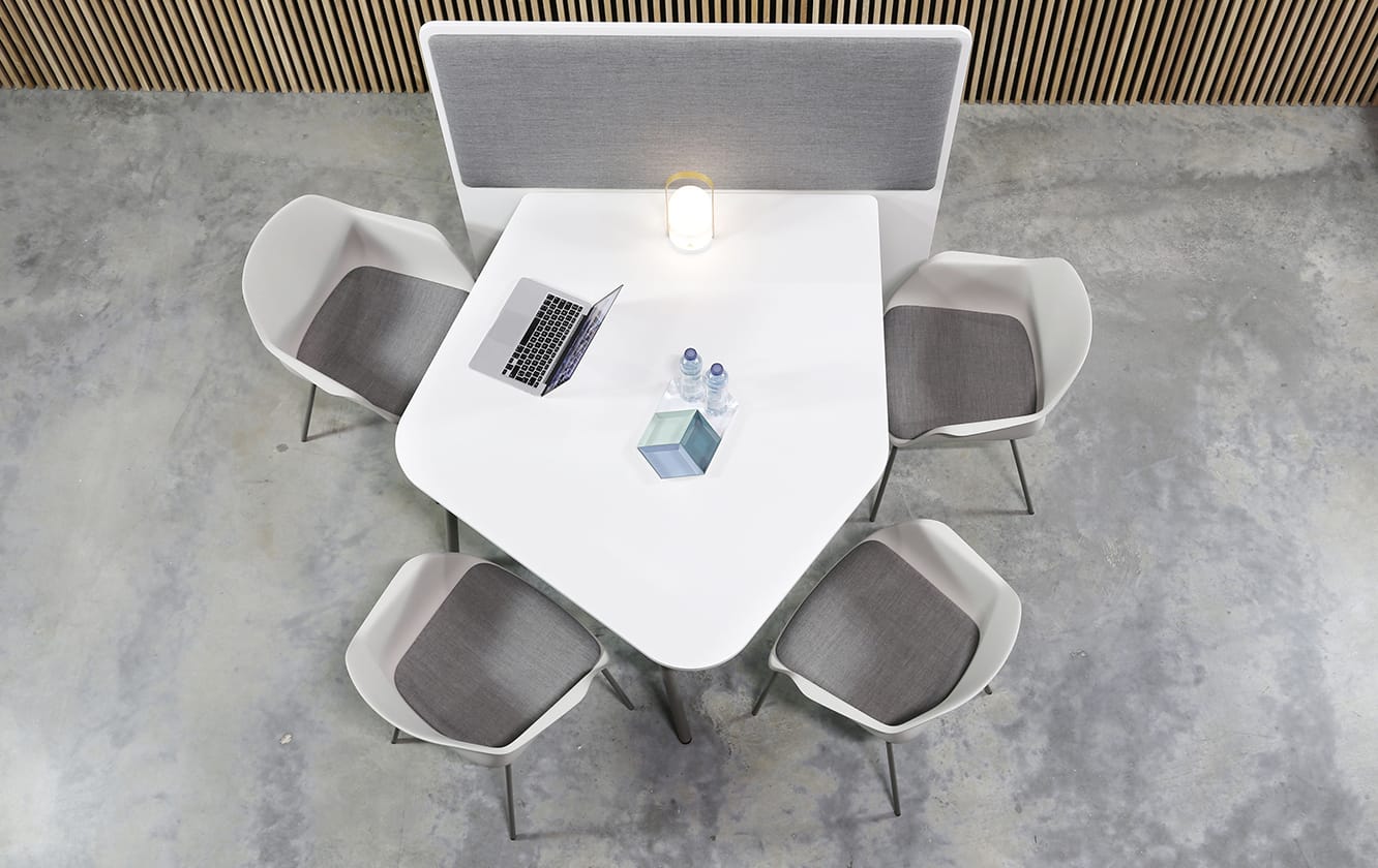 A white conference table with office screen divider attached with chairs and a laptop.
