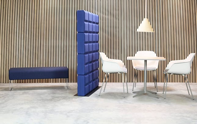 A blue chair and table in a room with wooden walls and a blue office screen divider