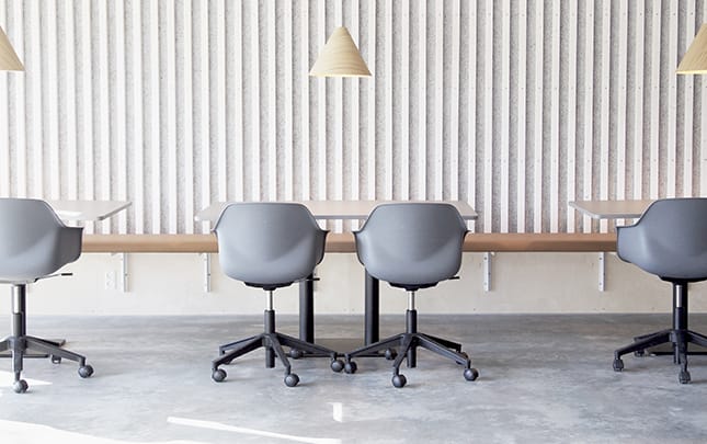 A group of grey chairs in an office with a white wall and a wall mounted bench on it.