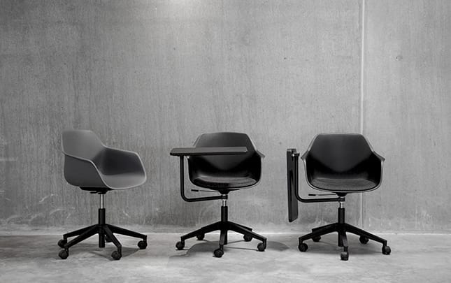 Three grey office chairs with desks attached in front of a concrete wall.