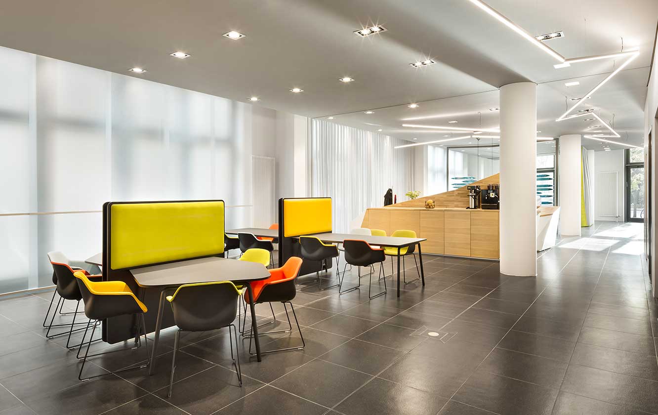 A brightly coloured office full of office furniture with tables and chairs.