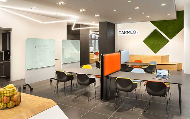 A modern office with orange chairs and office screen dividers and tables.