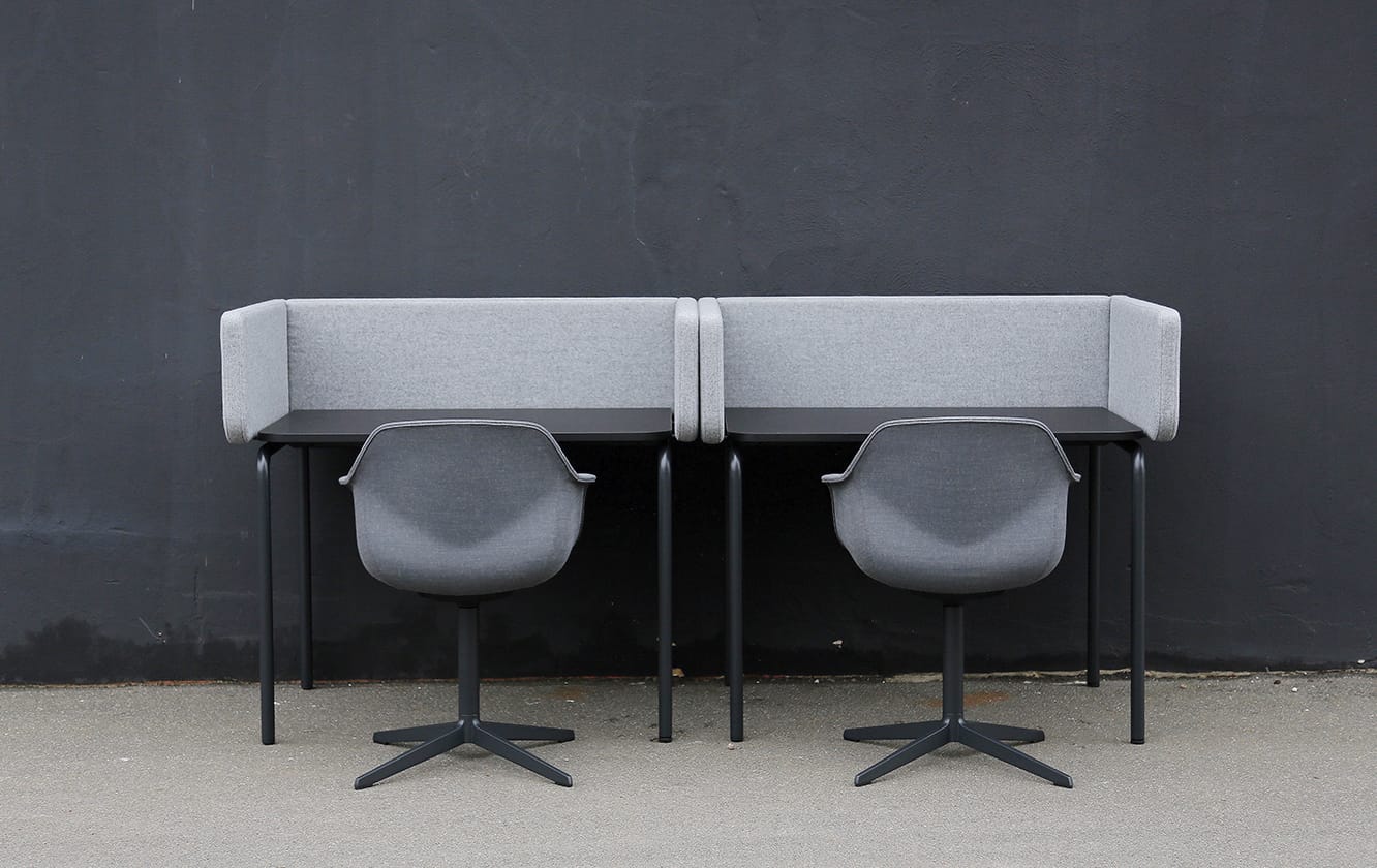 Two grey chairs in front of desk workstations in front of a black wall.