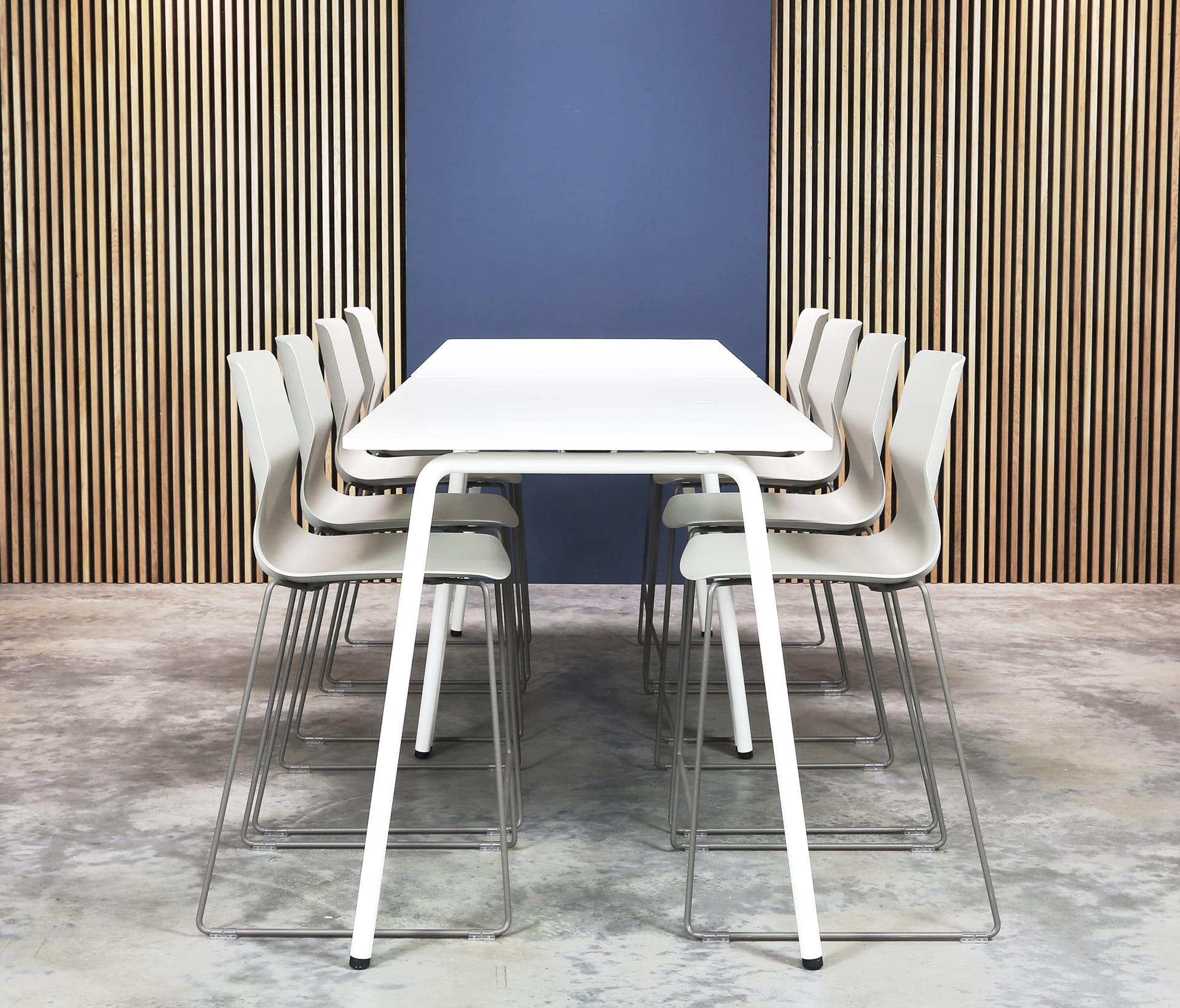 A white table and counter chairs in front of a wooden wall.