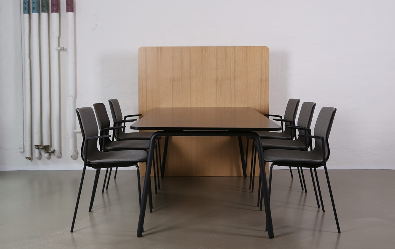 A table with an office screen dividers and chairs in a room with a wooden wall.