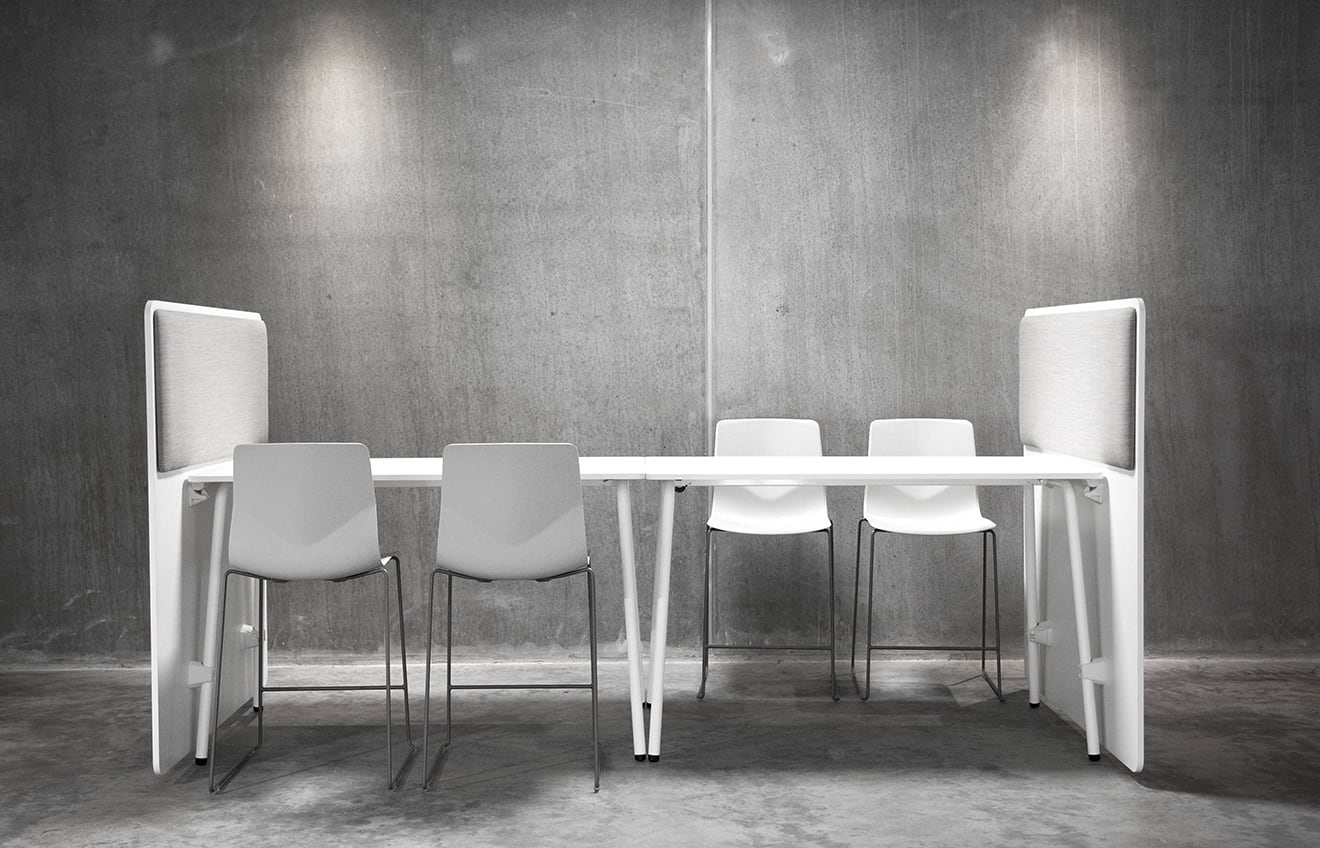 A white table with office screen dividers and chairs in a concrete room.