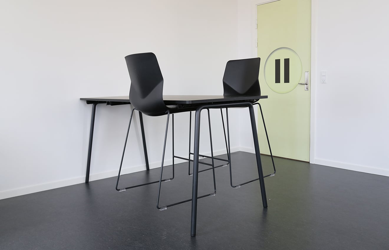 Two black counter chairs and a standing height table in an empty room.