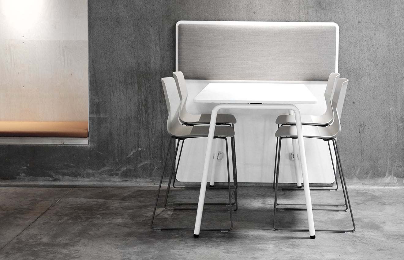 A white standing height table and chairs in a concrete room.