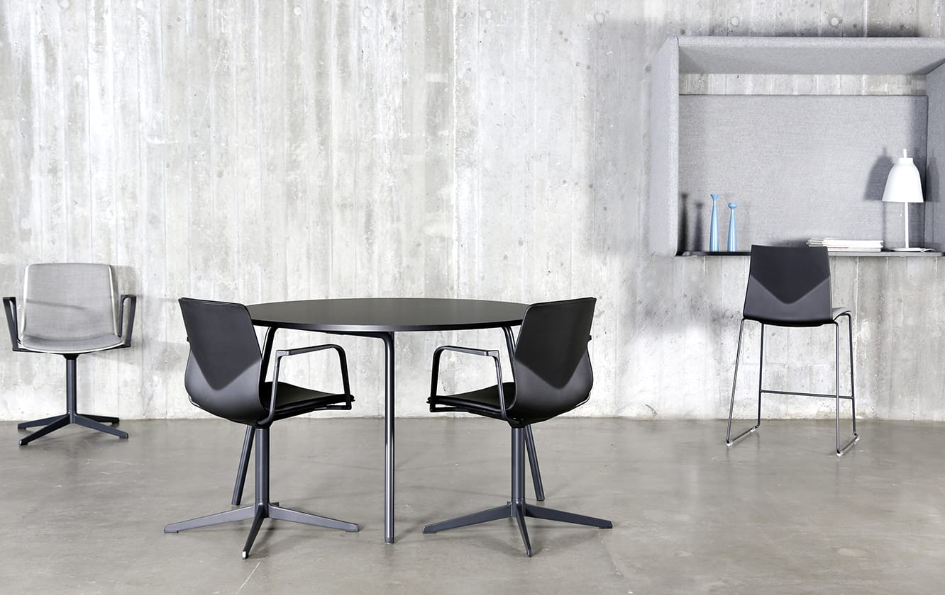 Four chairs and a table in a room with a wall mounted desk workstation on a concrete wall.