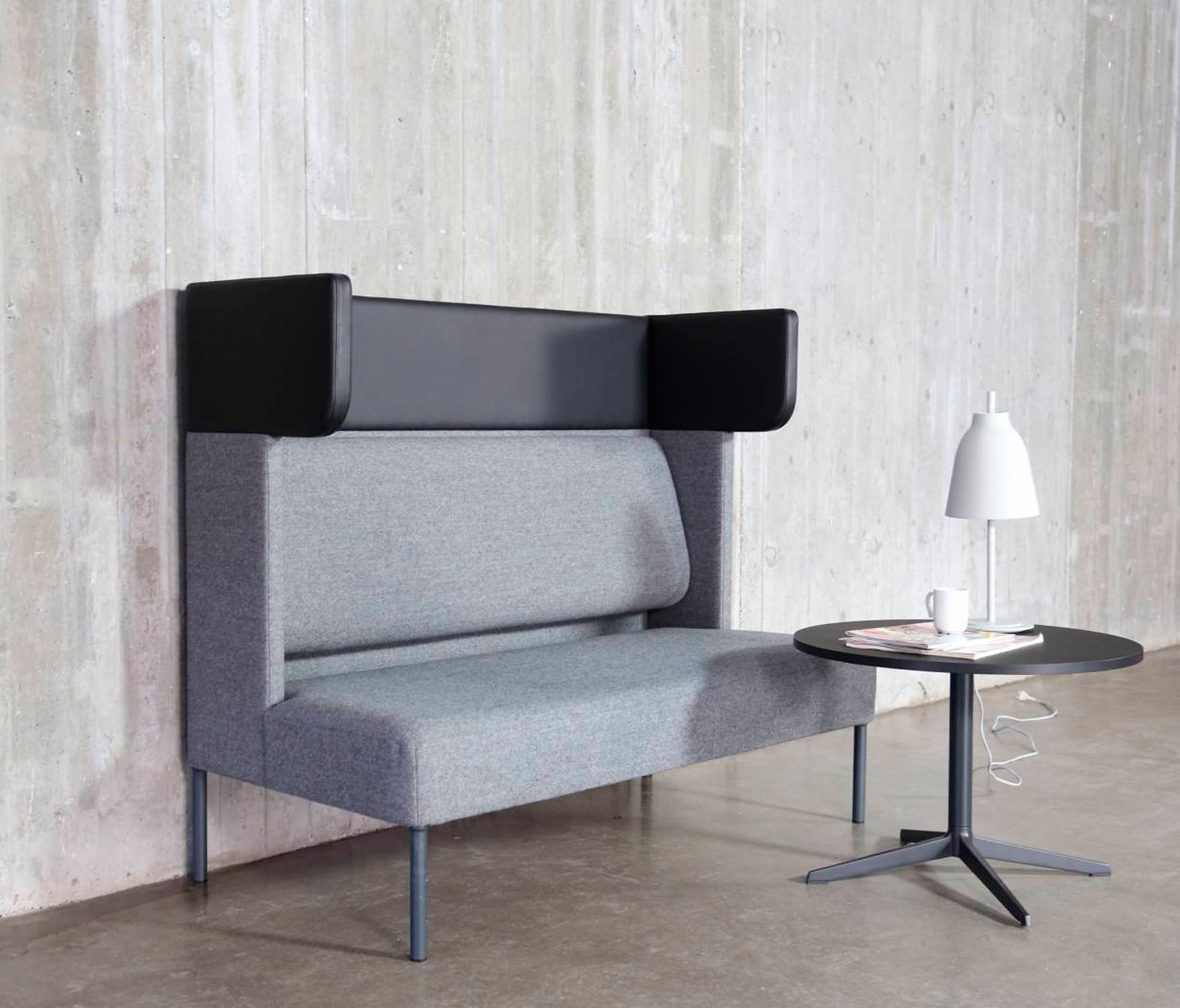 A grey couch with a table and lamp in front of a concrete wall.
