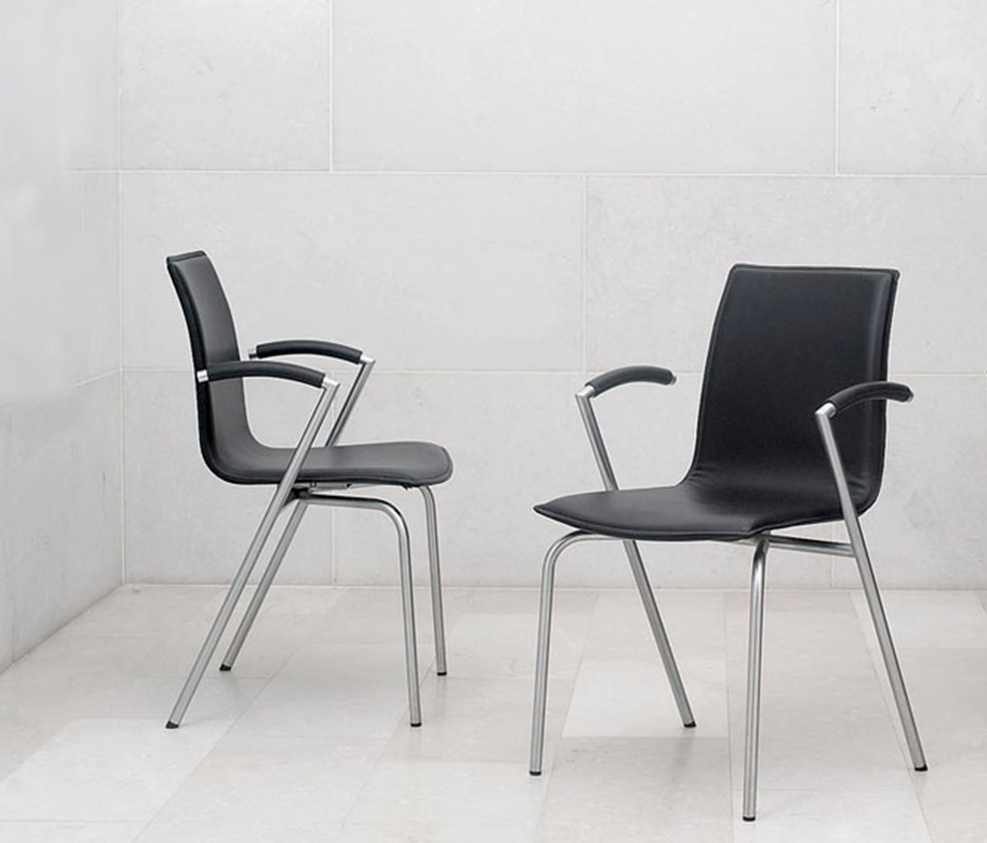Two black leather office desk chairs in front of a white wall.