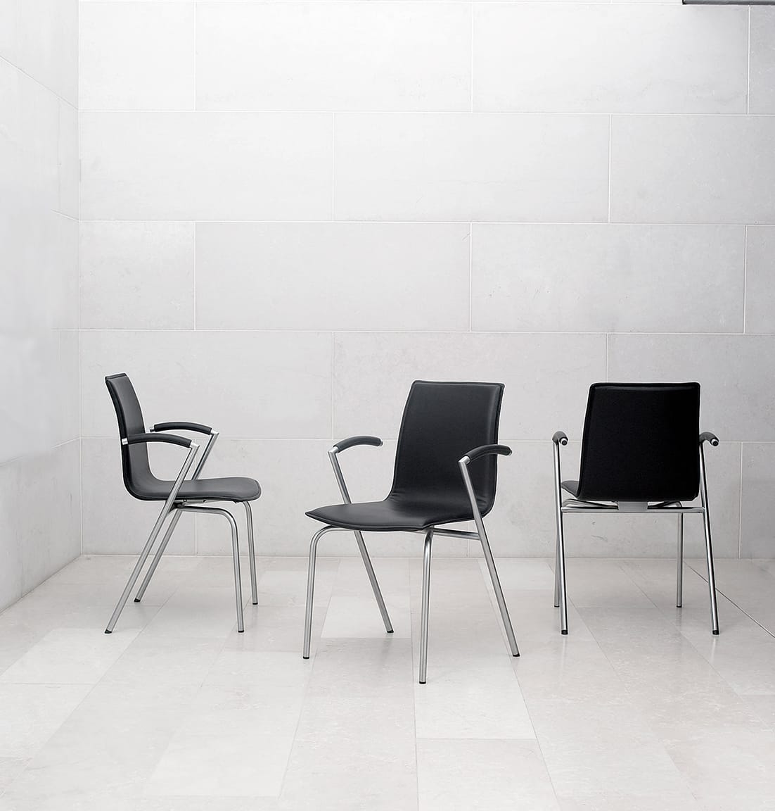 Three black office desk chairs in front of a white wall.