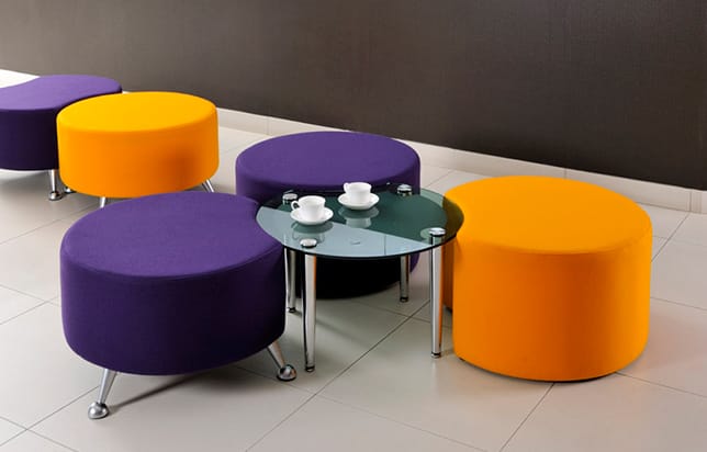 A group of colourful office stools with a glass office coffee table in the middle of them