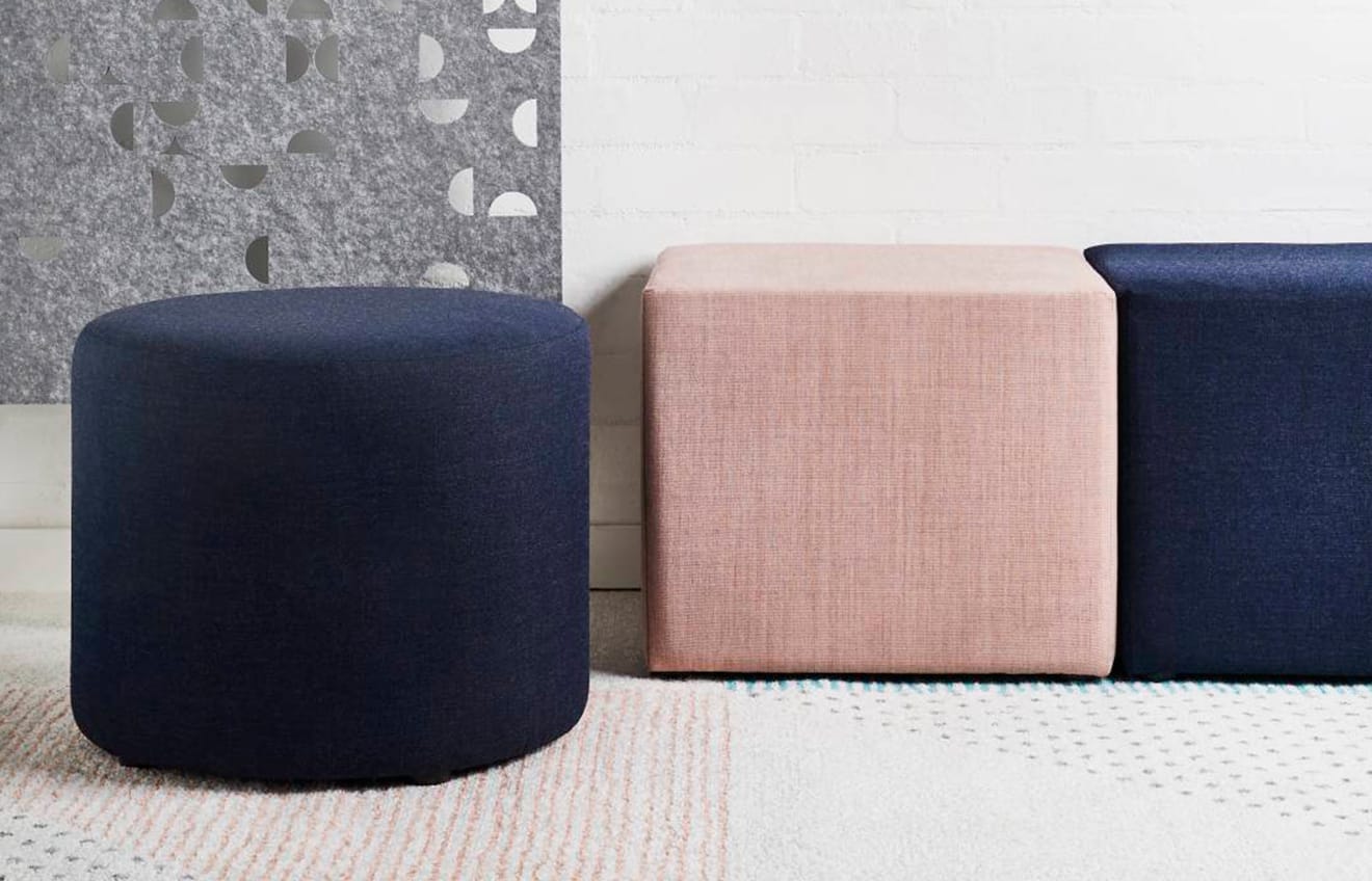 A blue, pink, and grey ottoman in front of a white wall.