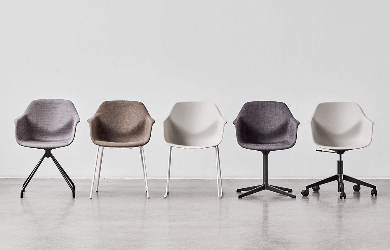 Five chairs in a row against a white wall. Each one has a different seat material and leg configuration from pedestal to 4-legged