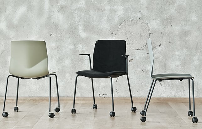 Three office desk chairs on wheels in front of a wall.