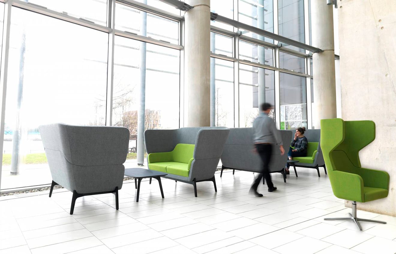 A group of people walking around office sofas in a large office.