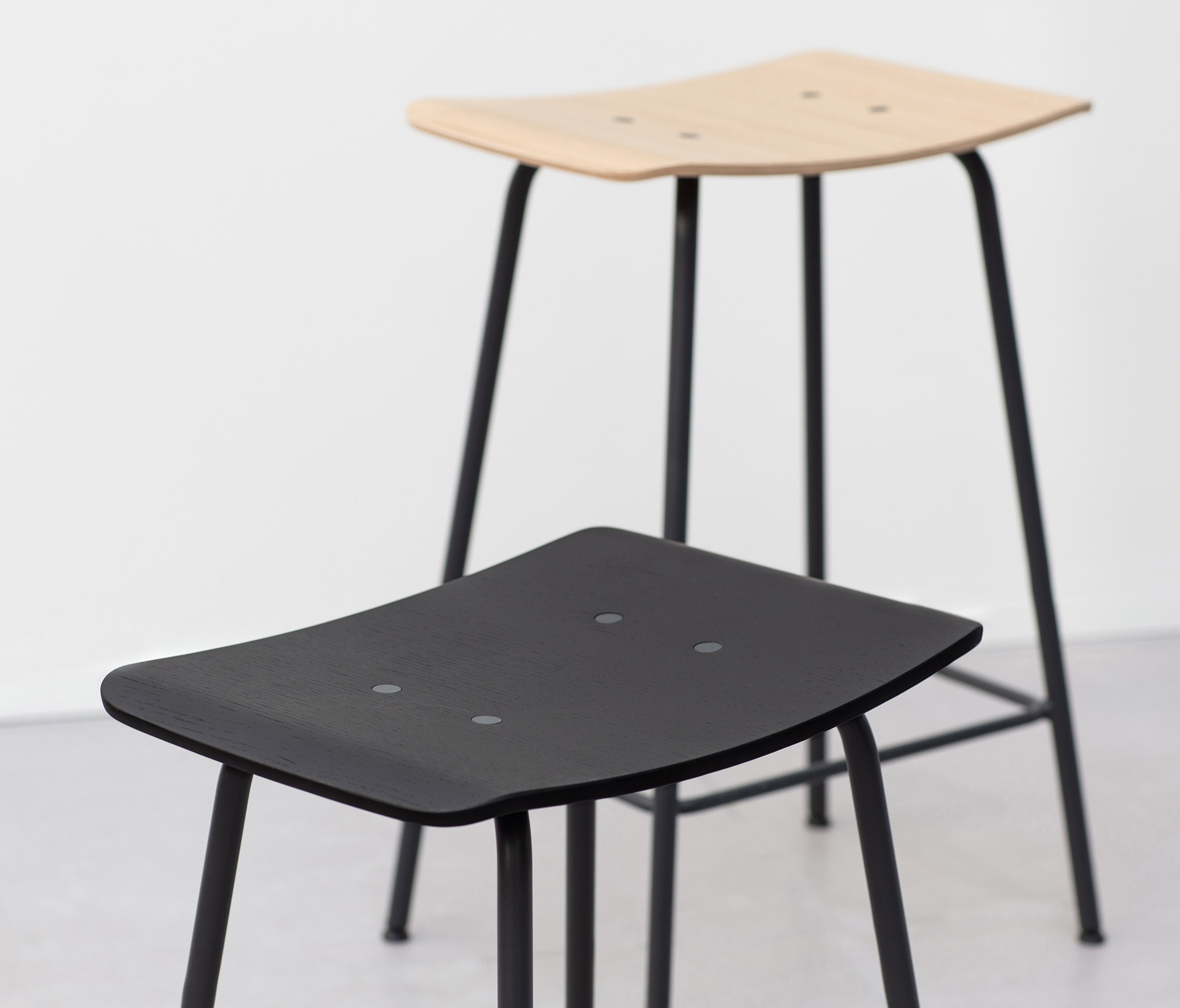 Two wooden Share office stools, one with a black seat and one with a wooden seat.