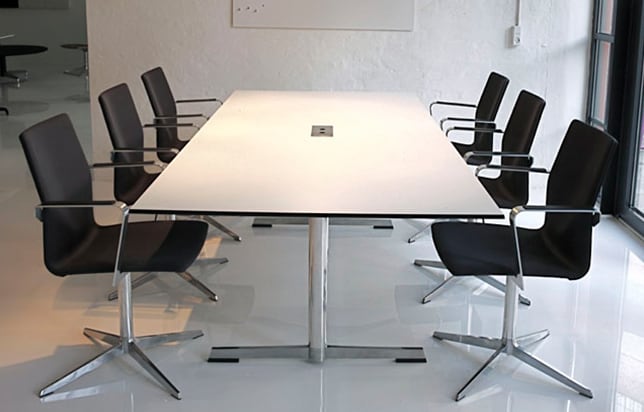 A white conference table with black chairs in an office.