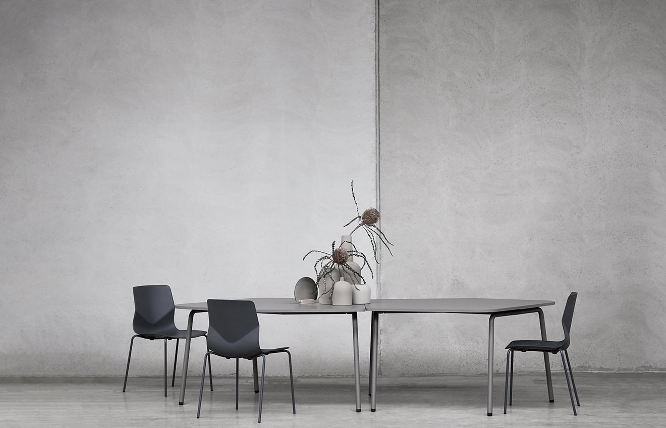 A dining table with four chairs in front of a concrete wall.