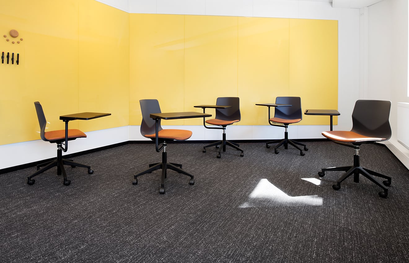A group of chairs with desks attached in a room with a yellow wall.