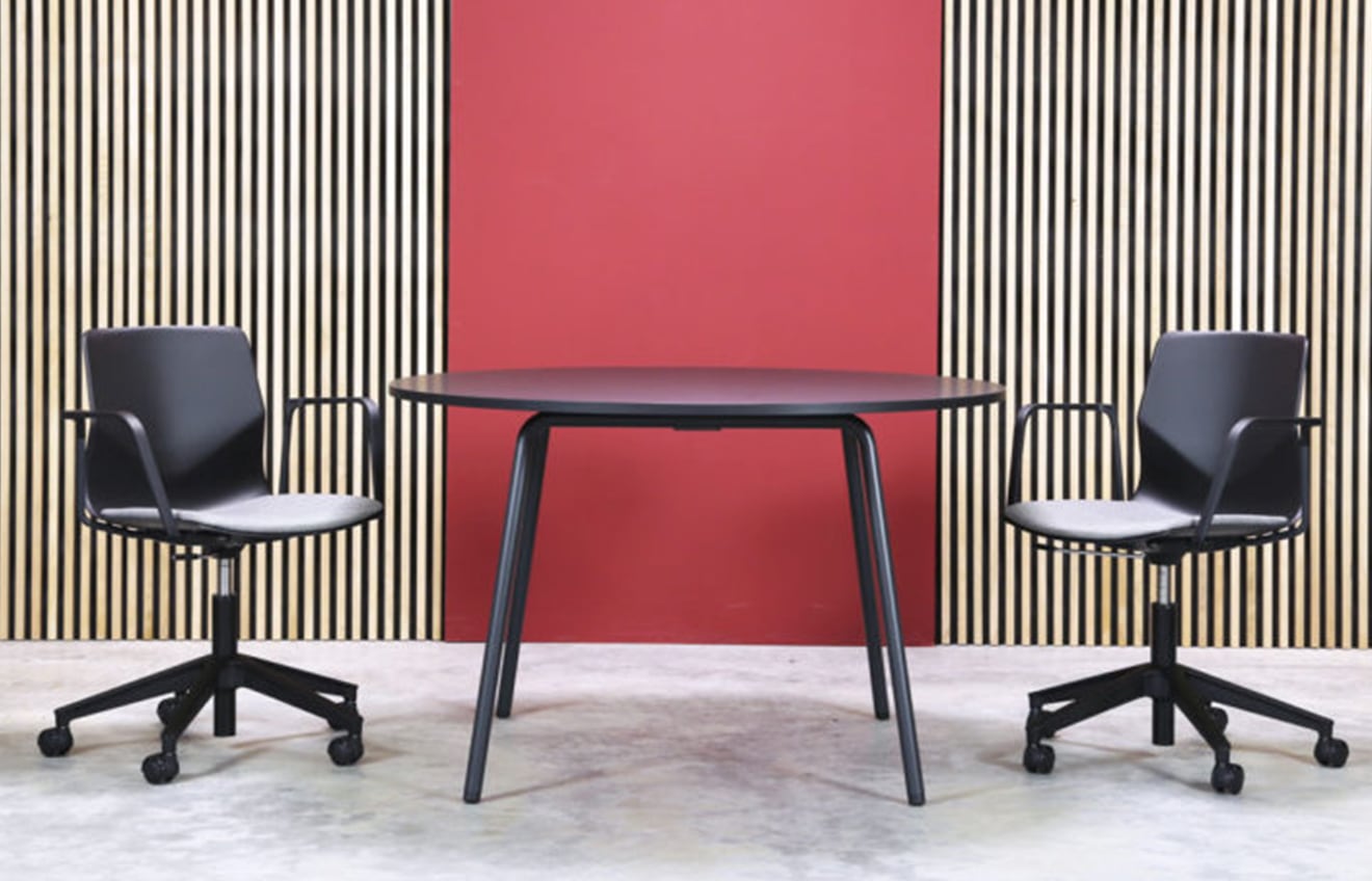 Two office desk chairs and a table in front of a red wall.