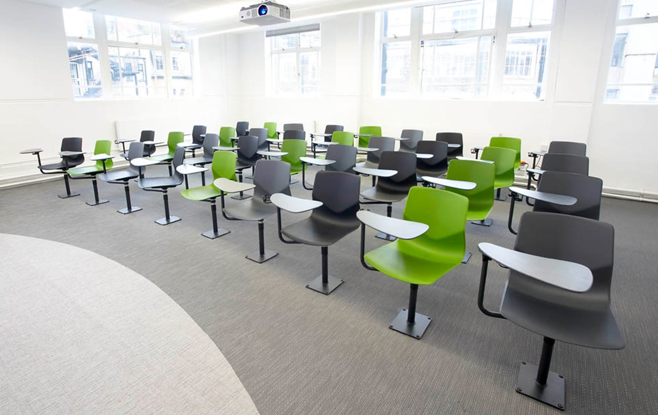 A classroom with green chairs with desk attached and a projector