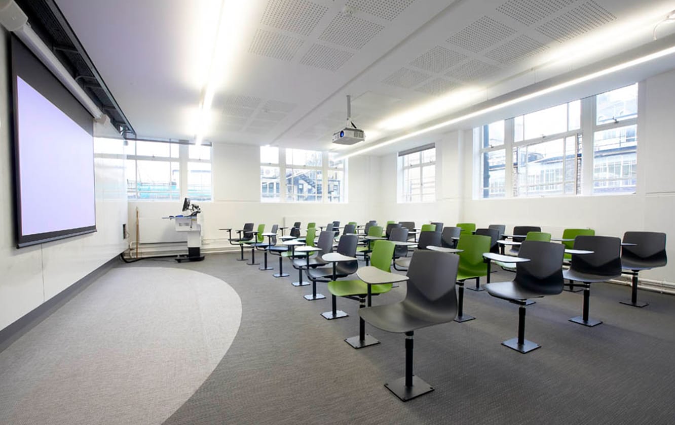 A classroom with green chairs with desk attached and a projector screen.