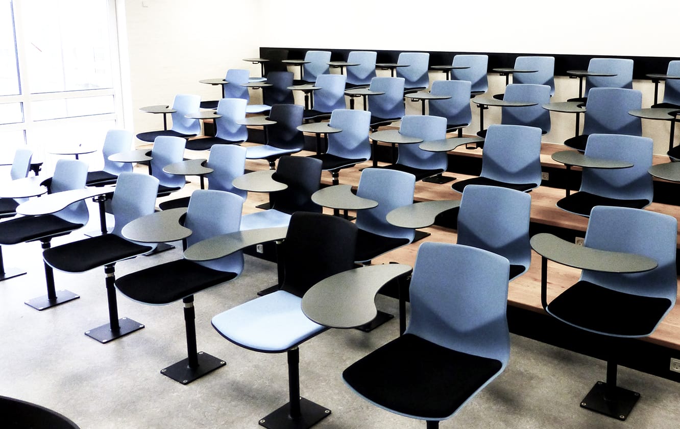 A classroom with blue chairs with desk attached