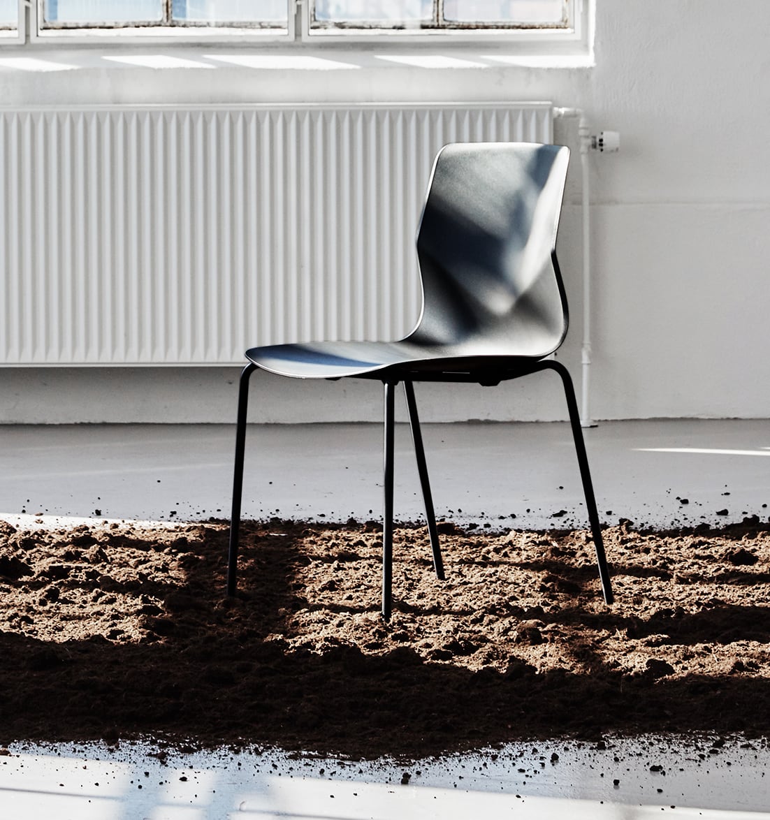 A black chair sits in the dirt in front of a window.
