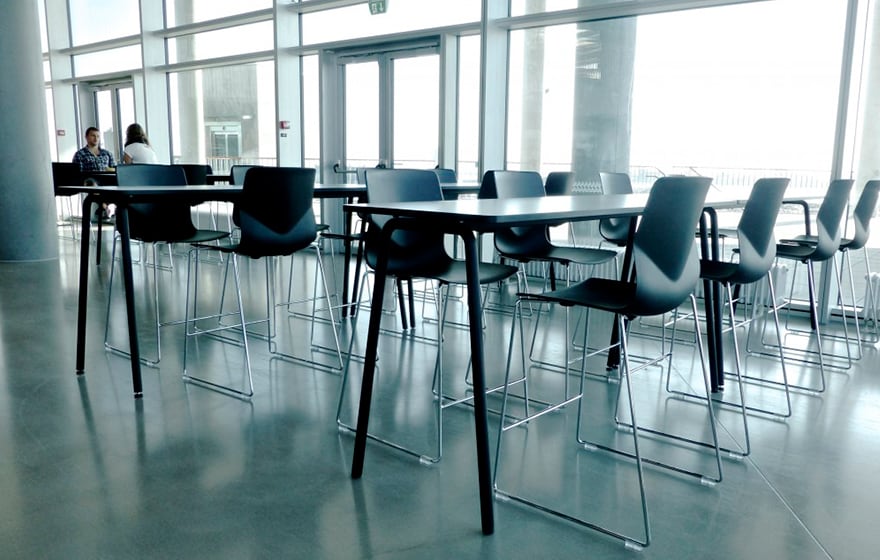 A group of black counter chairs around standing height tables in a conference room.