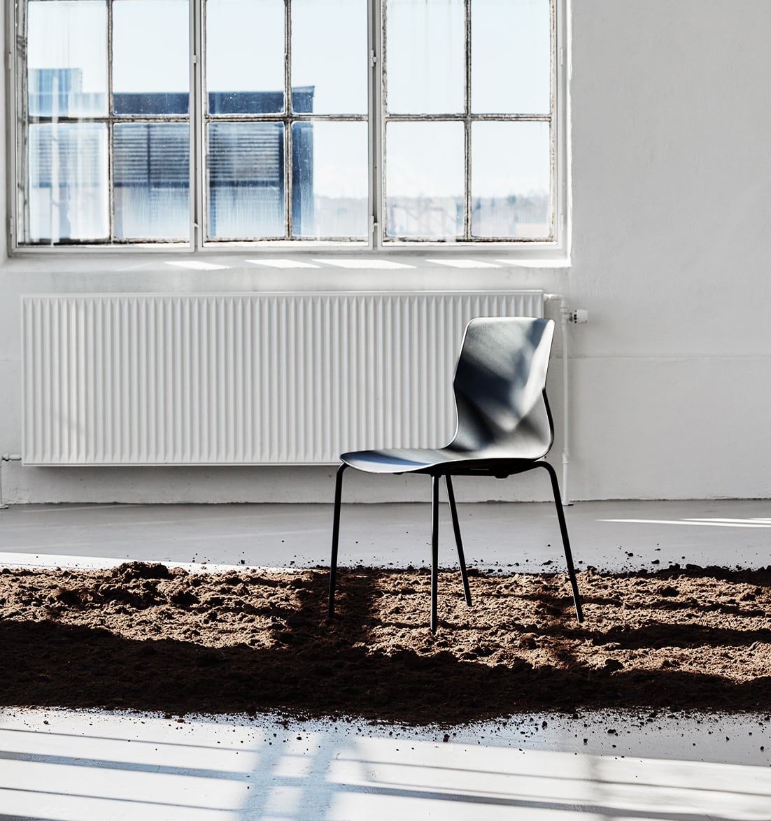A black chair sits on a dirt floor in front of a window.