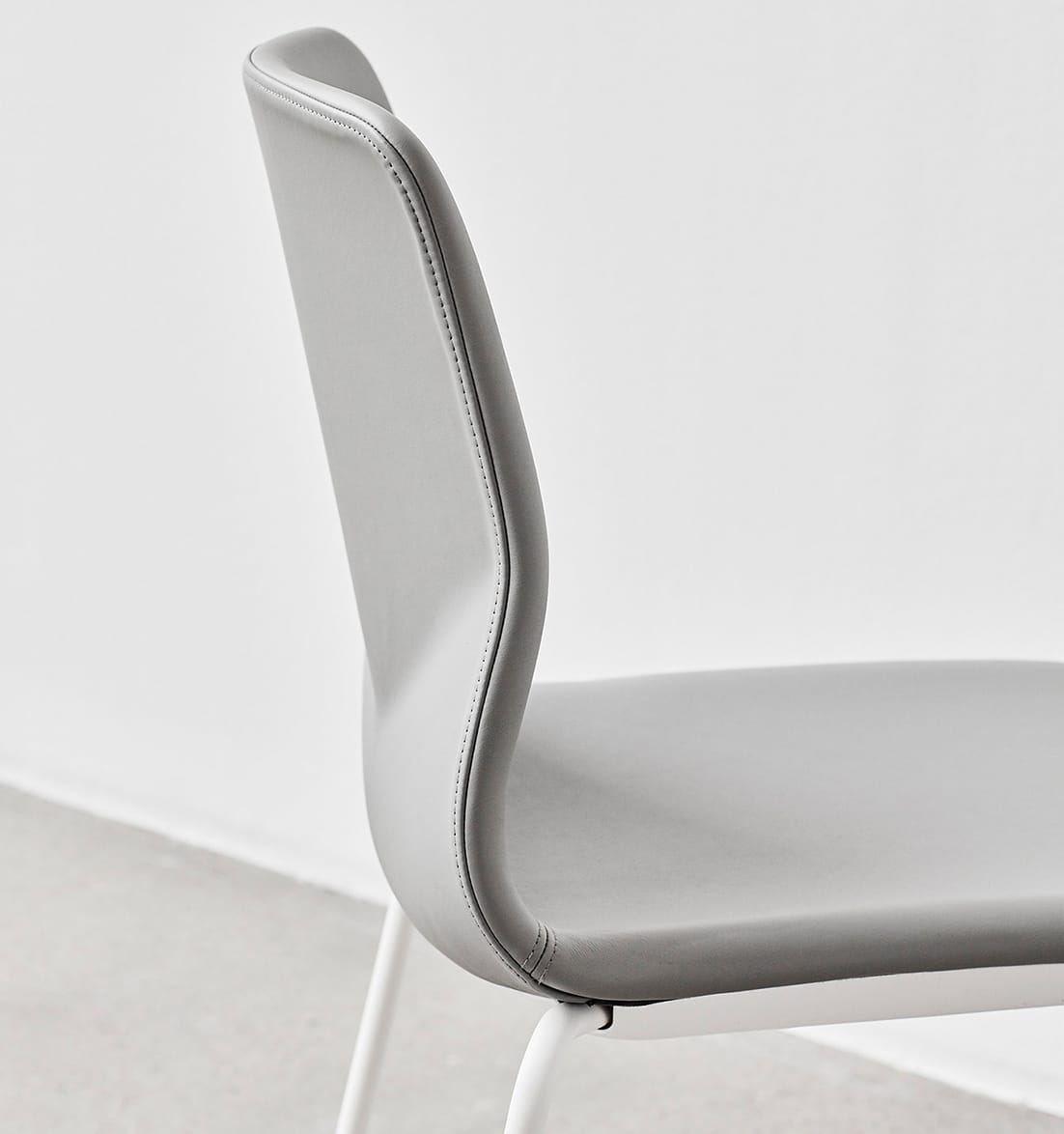 A grey chair with a white frame against a white wall.