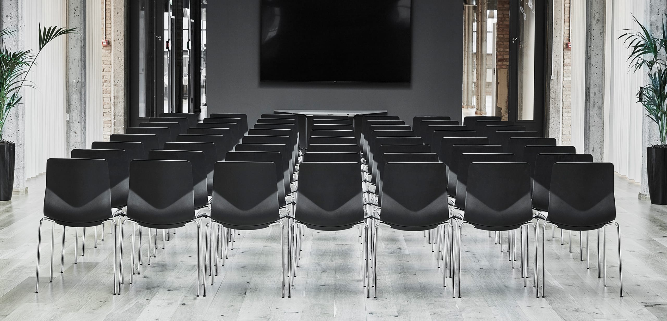 A row of black office desk chairs in a conference room with a tv.