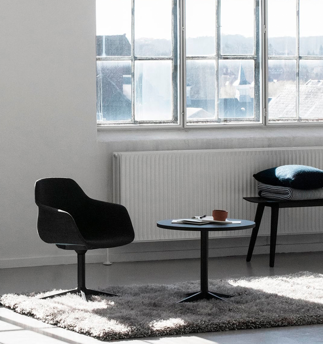 A black office desk chair in front of a window in a living room.