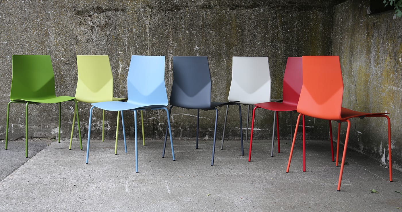 A group of colourful chairs in front of a concrete wall.