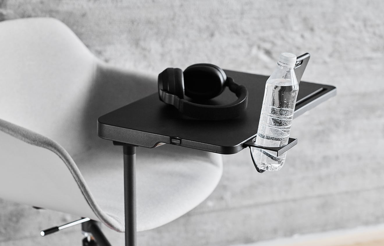 A white chair with black desk attached with headphones and a bottle of water.
