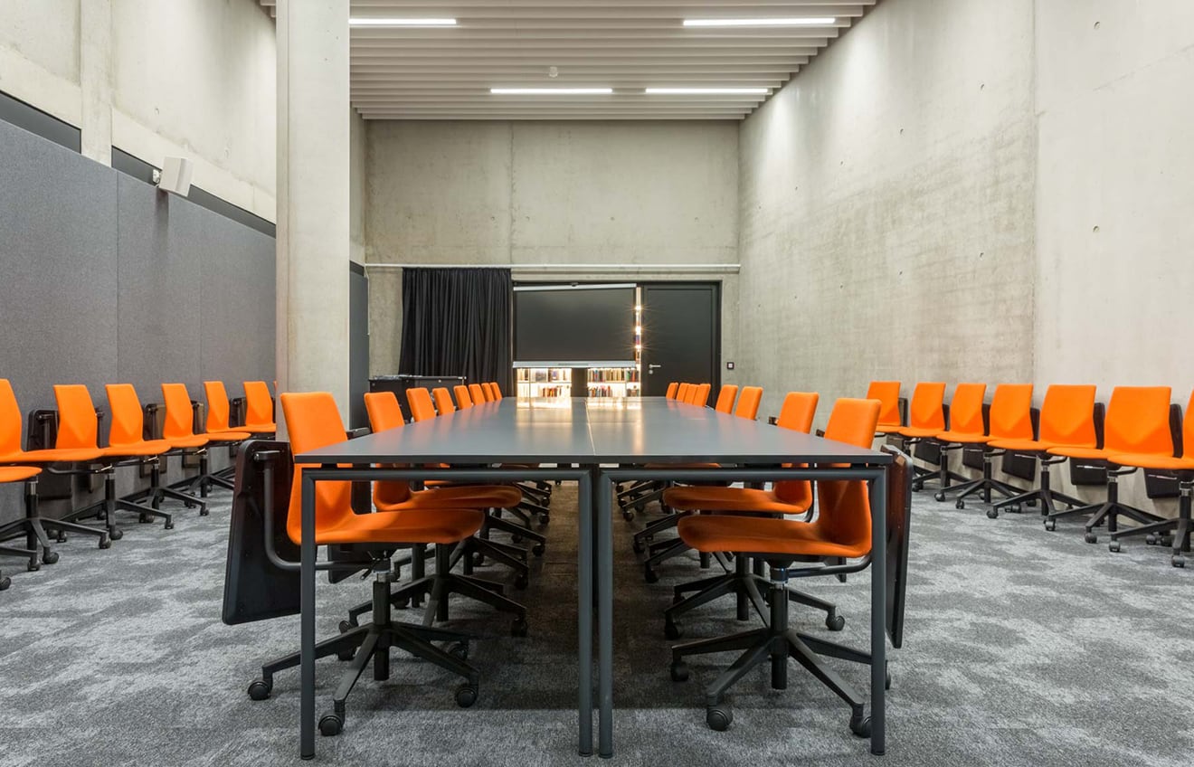 A conference room with orange desk chairs chairs and a long table.