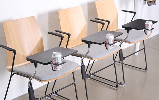 A row of chairs with desk attached with cans on them.