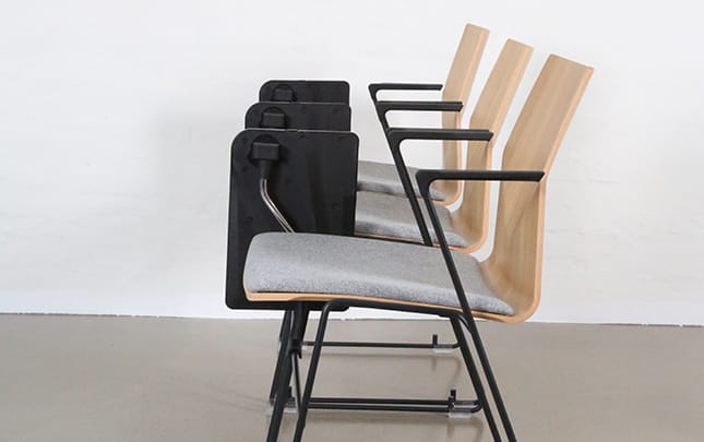 Four chairs with desk attached with a black frame and a black seat with desk folded down
