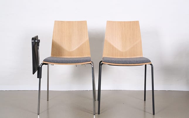 Two wooden chairs with a grey upholstered seat. One has a desk attached that is folded down