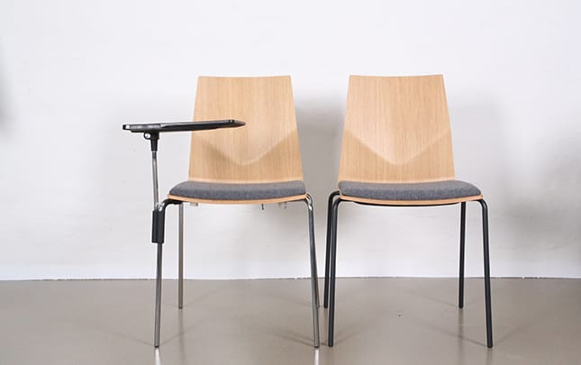 Two wooden chairs with a grey upholstered seat. One has a desk attached.